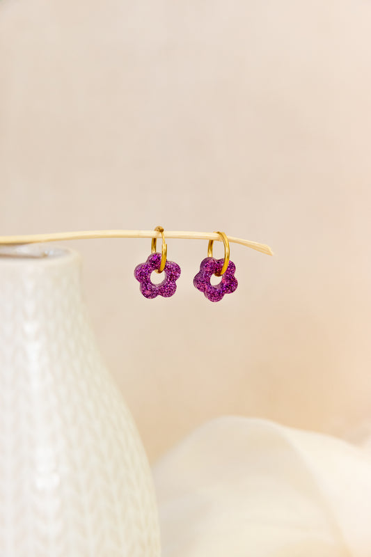 Pair of purple flower-shaped earrings on a beige background