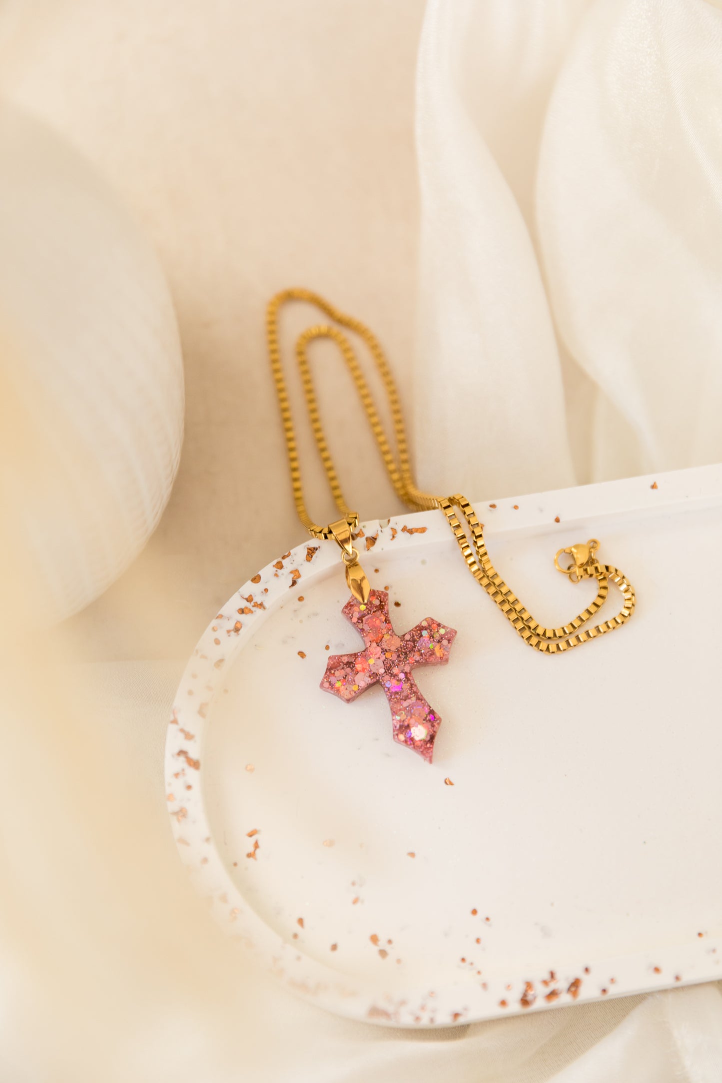 Necklace with a pink cross pendant on a white shell against a beige background