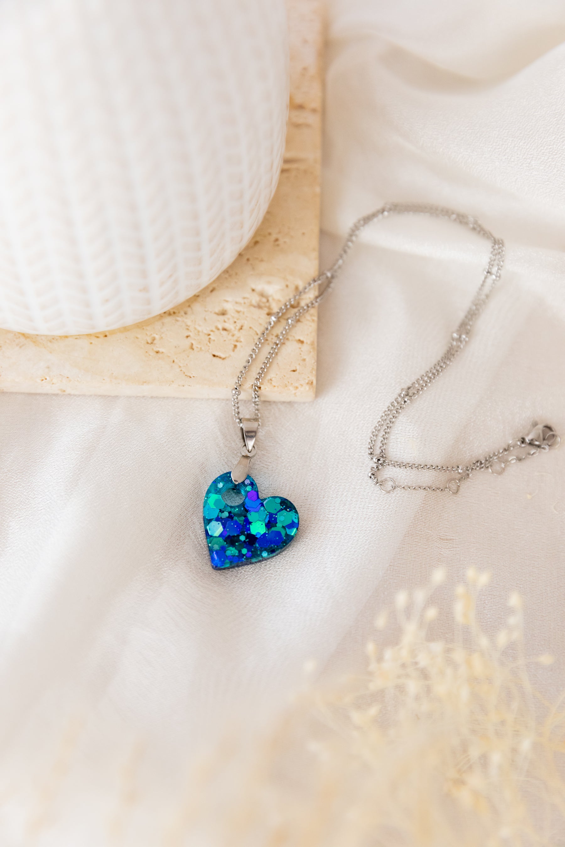 Heart-shaped blue pendant on a chain against a soft beige background