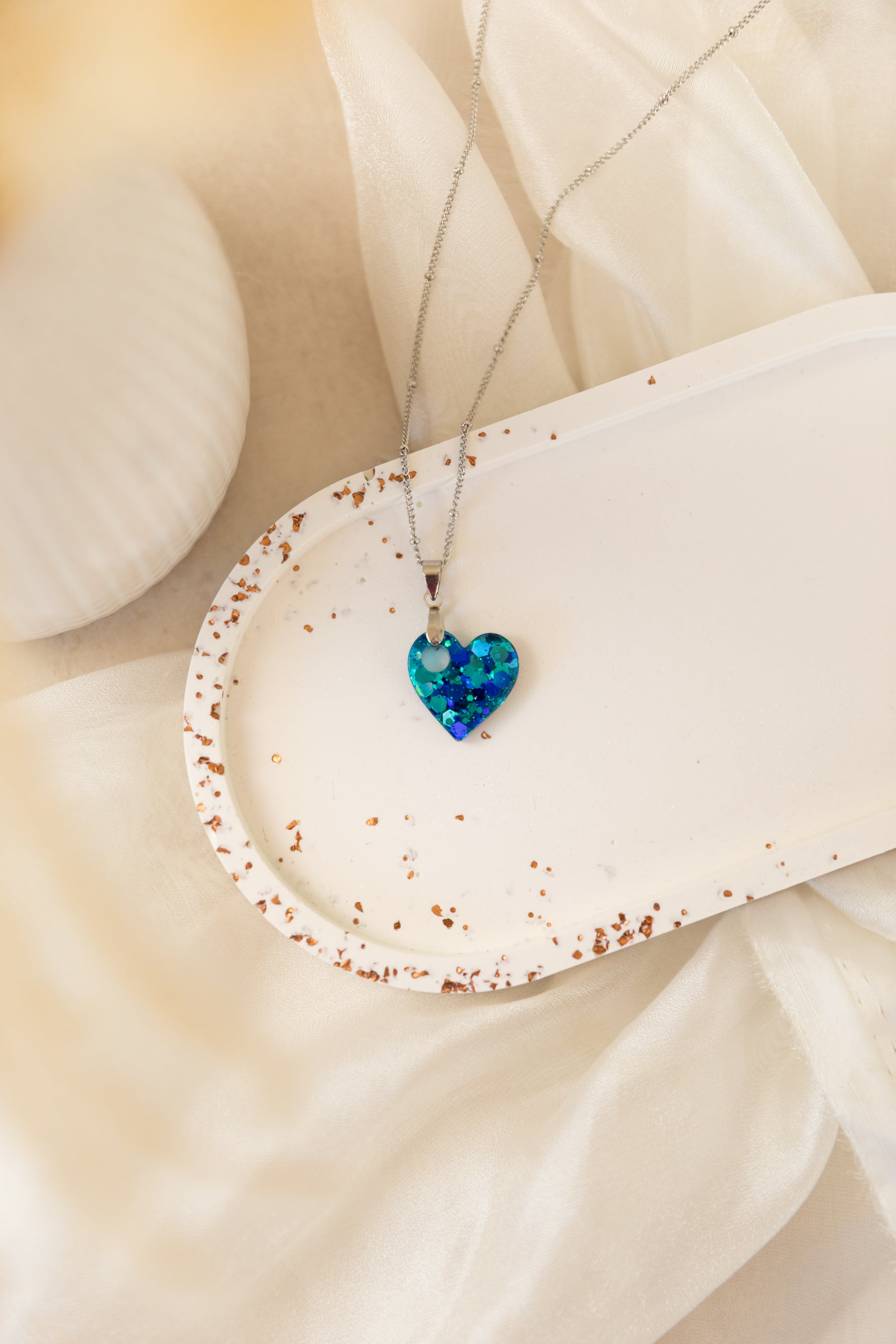Heart-shaped blue pendant on a necklace against a beige fabric background