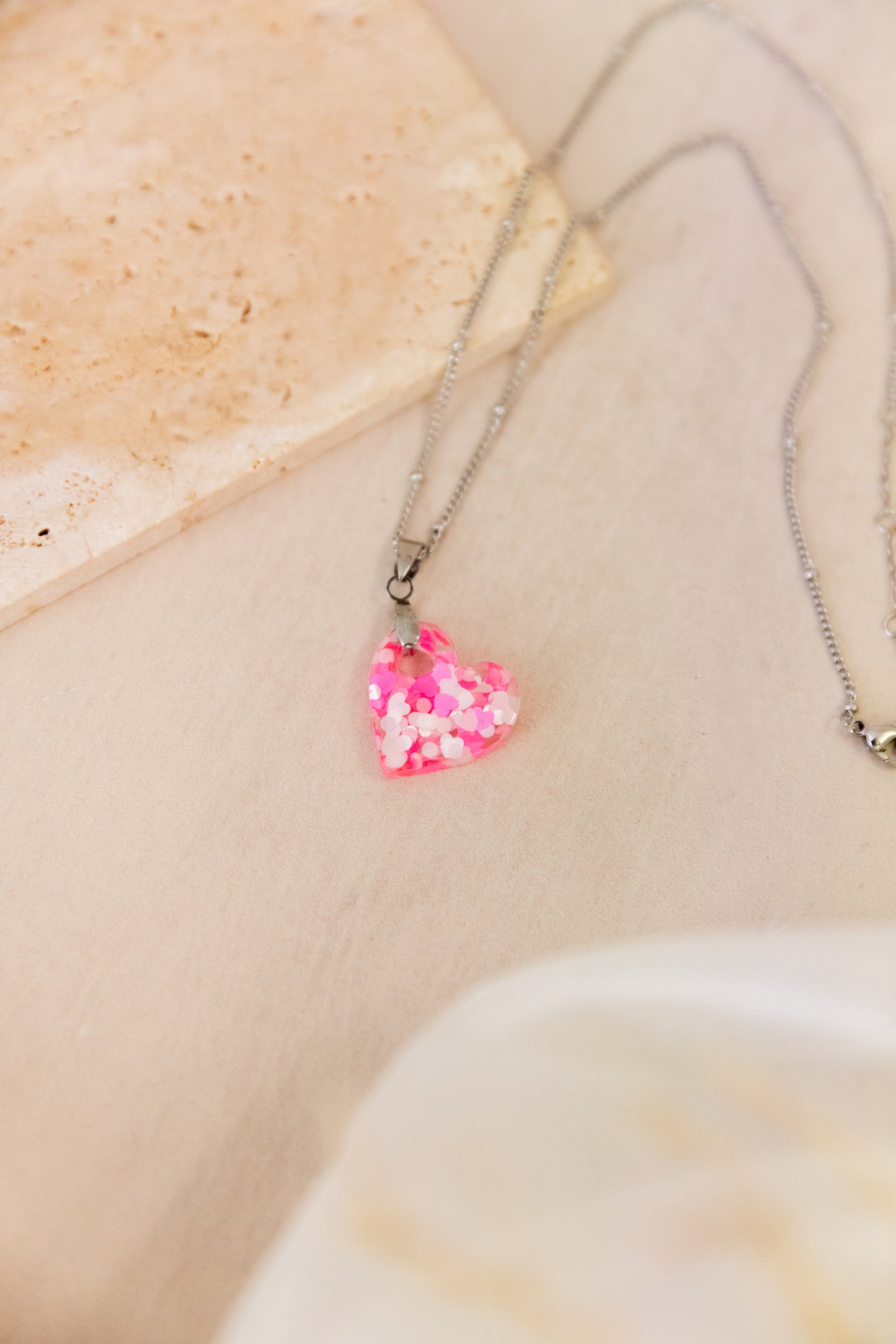 Necklace with a pink heart-shaped pendant on a beige stone background