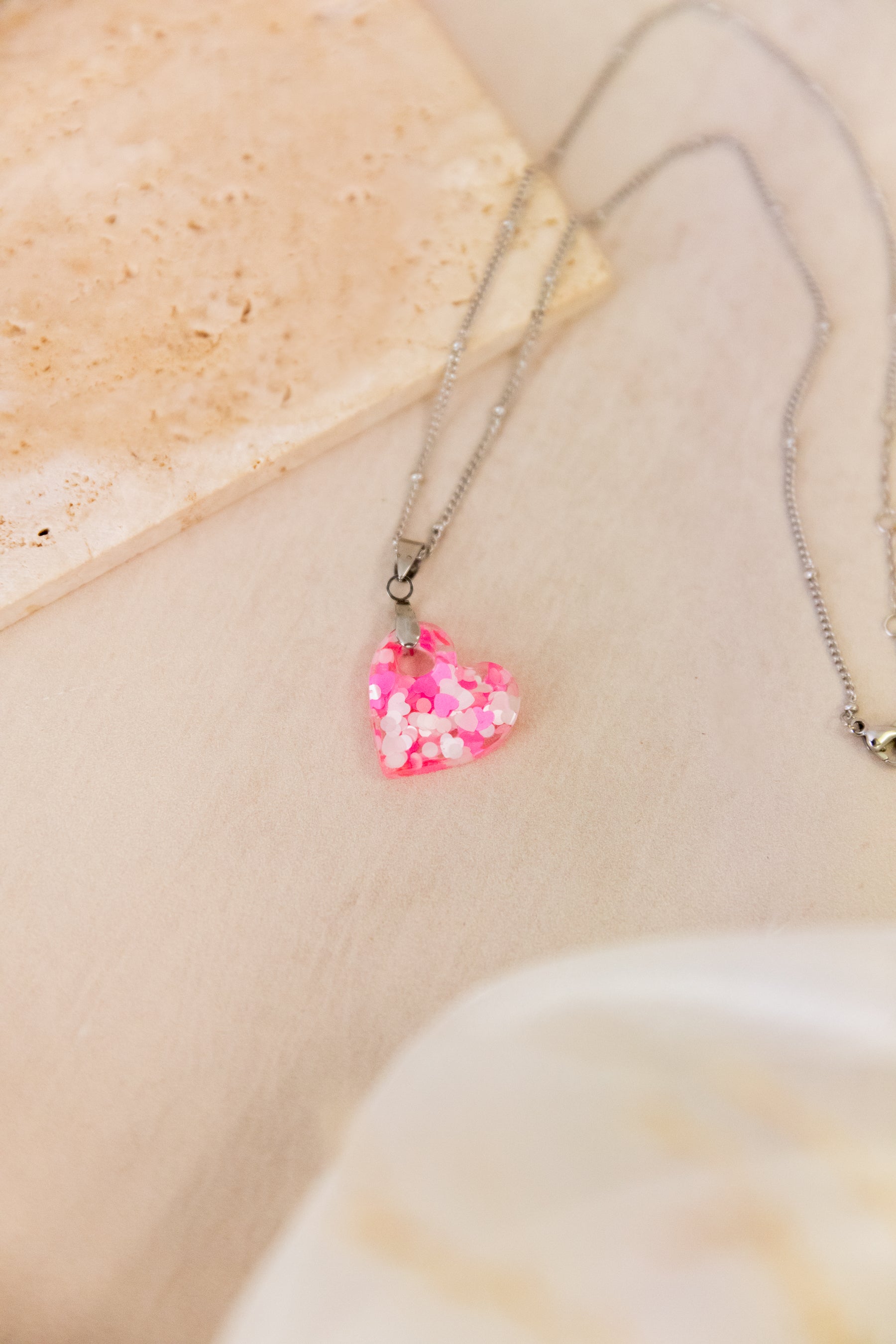 Necklace with a pink heart-shaped pendant on a beige stone background