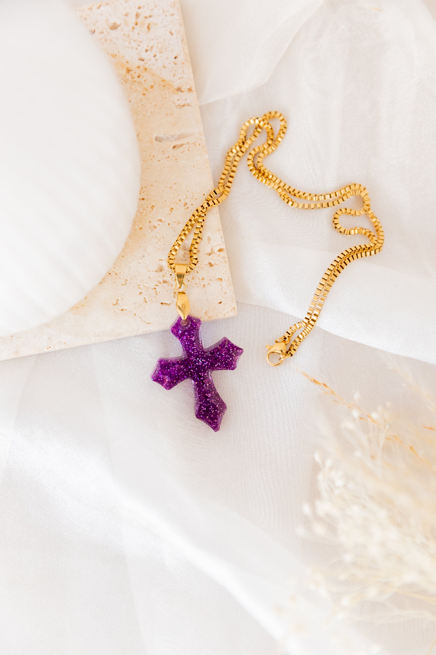 Gold necklace with a purple cross pendant on a white surface