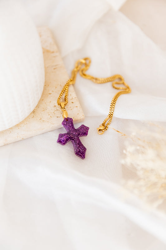 Purple cross pendant on a gold chain with a white background