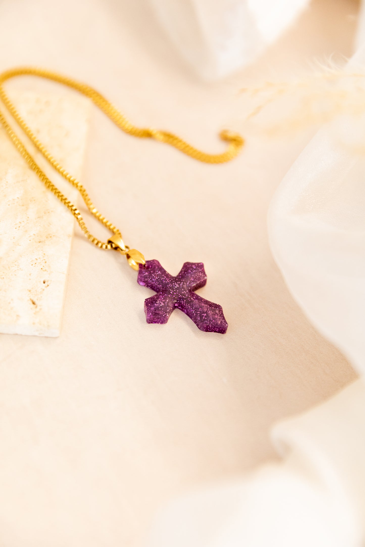 Purple cross pendant on a gold chain against a neutral background