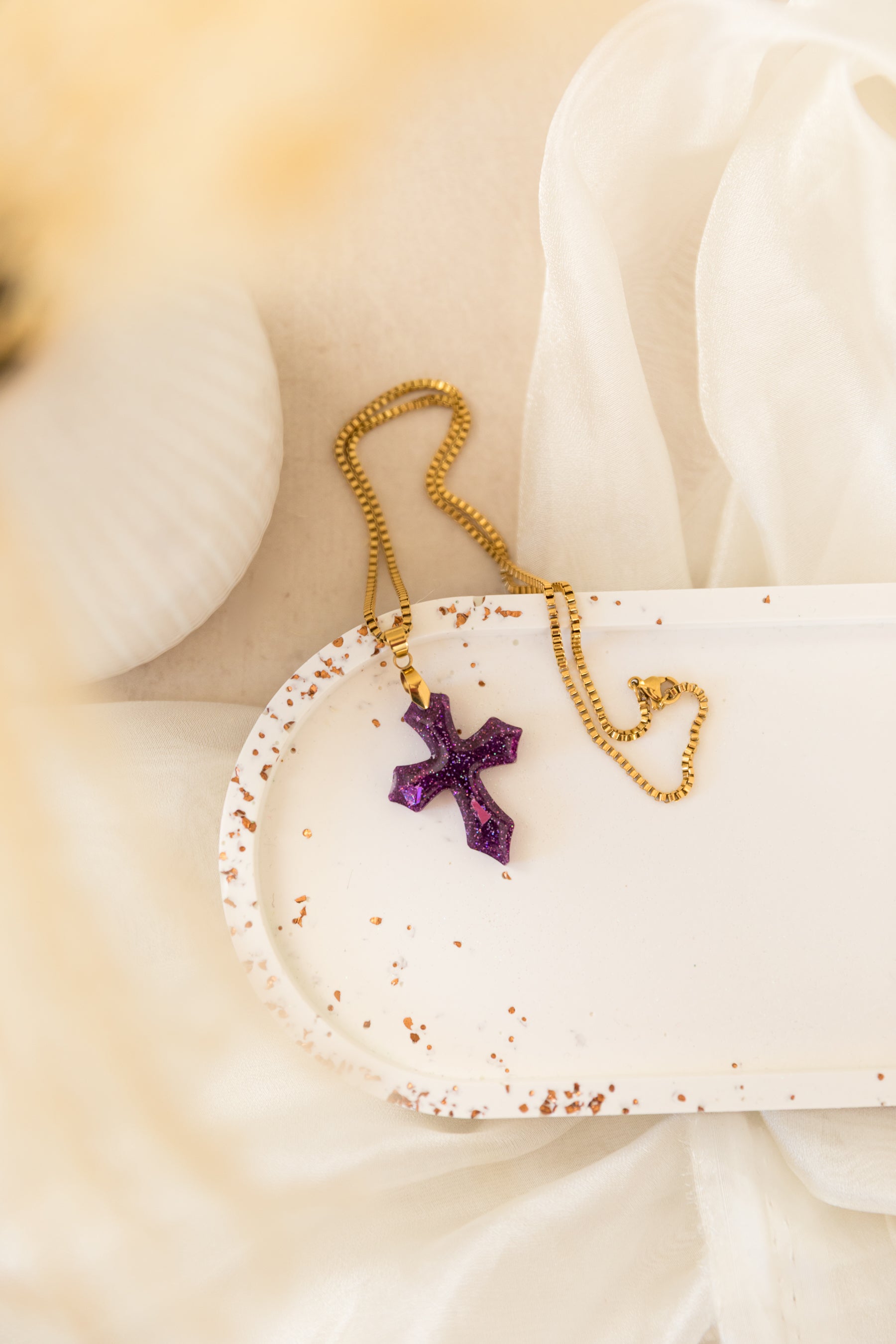 Gold necklace with a purple cross pendant on a white surface