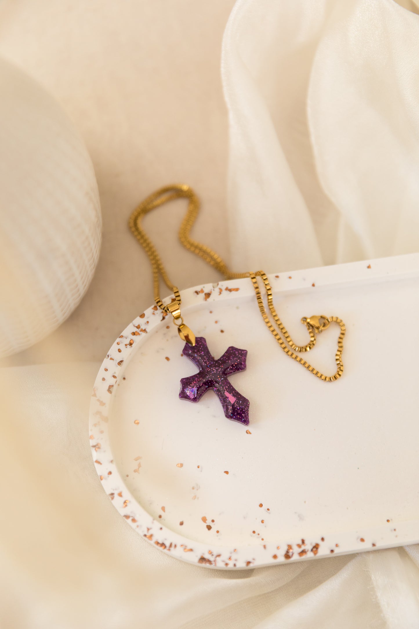 Necklace with a purple cross pendant on a white dish with gold chain