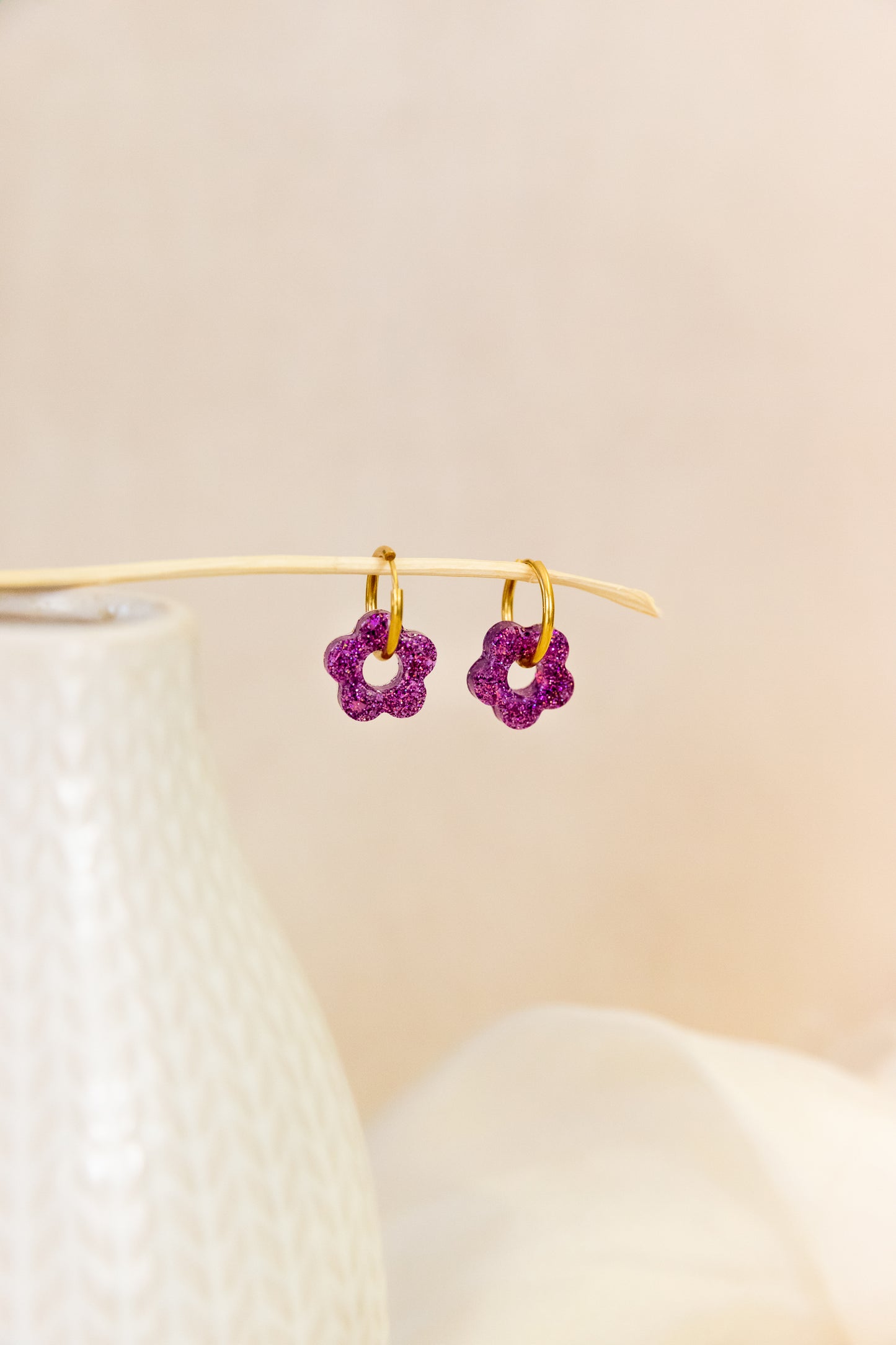 Pair of purple flower-shaped earrings on a beige background
