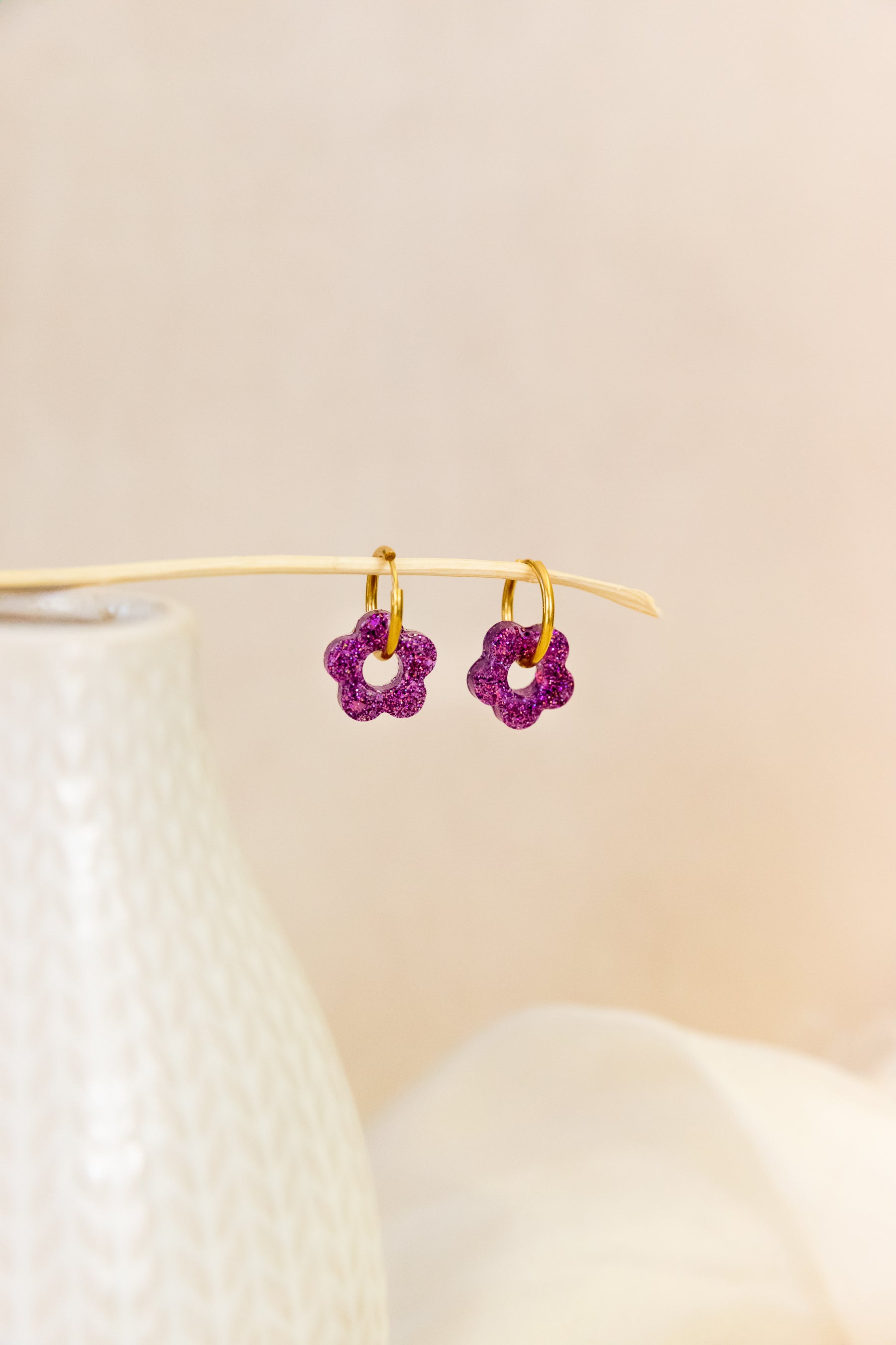 Pair of purple flower-shaped earrings on a beige background