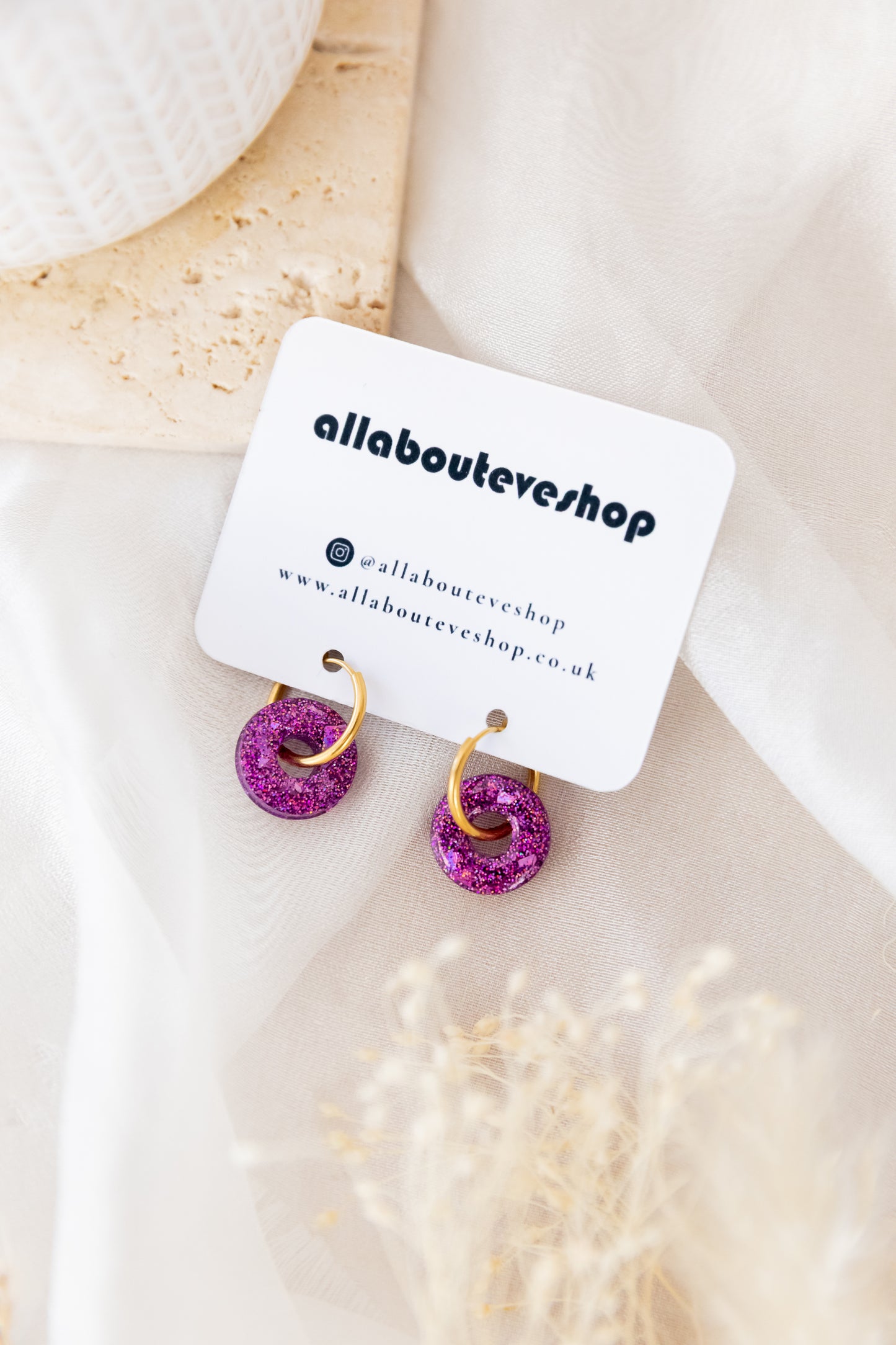 Pair of earrings with pink and gold details on a branded card, placed on a light surface.