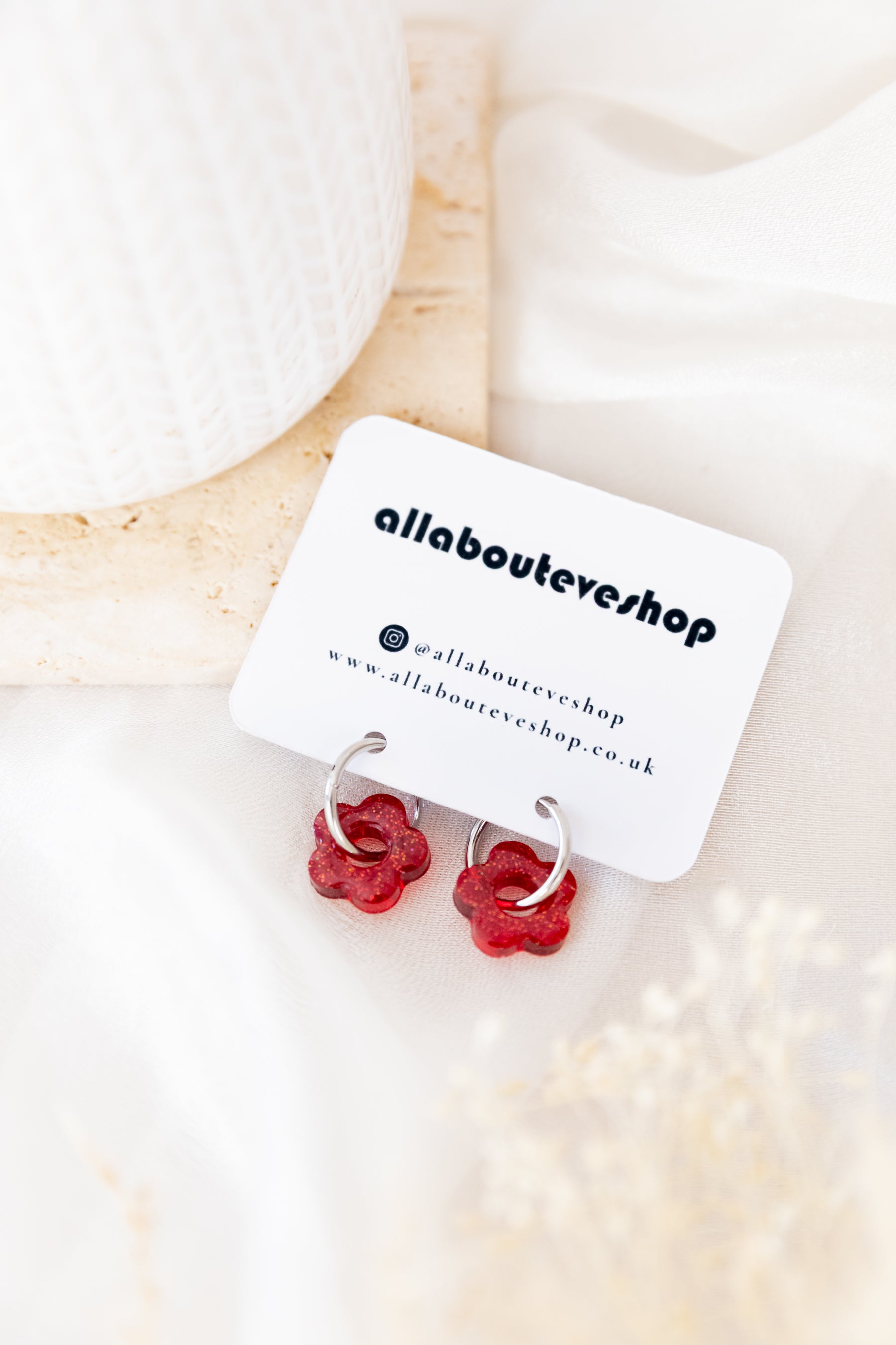 Red floral earrings on a white card with 'allabouteveryshop' branding, placed on a light wooden surface.