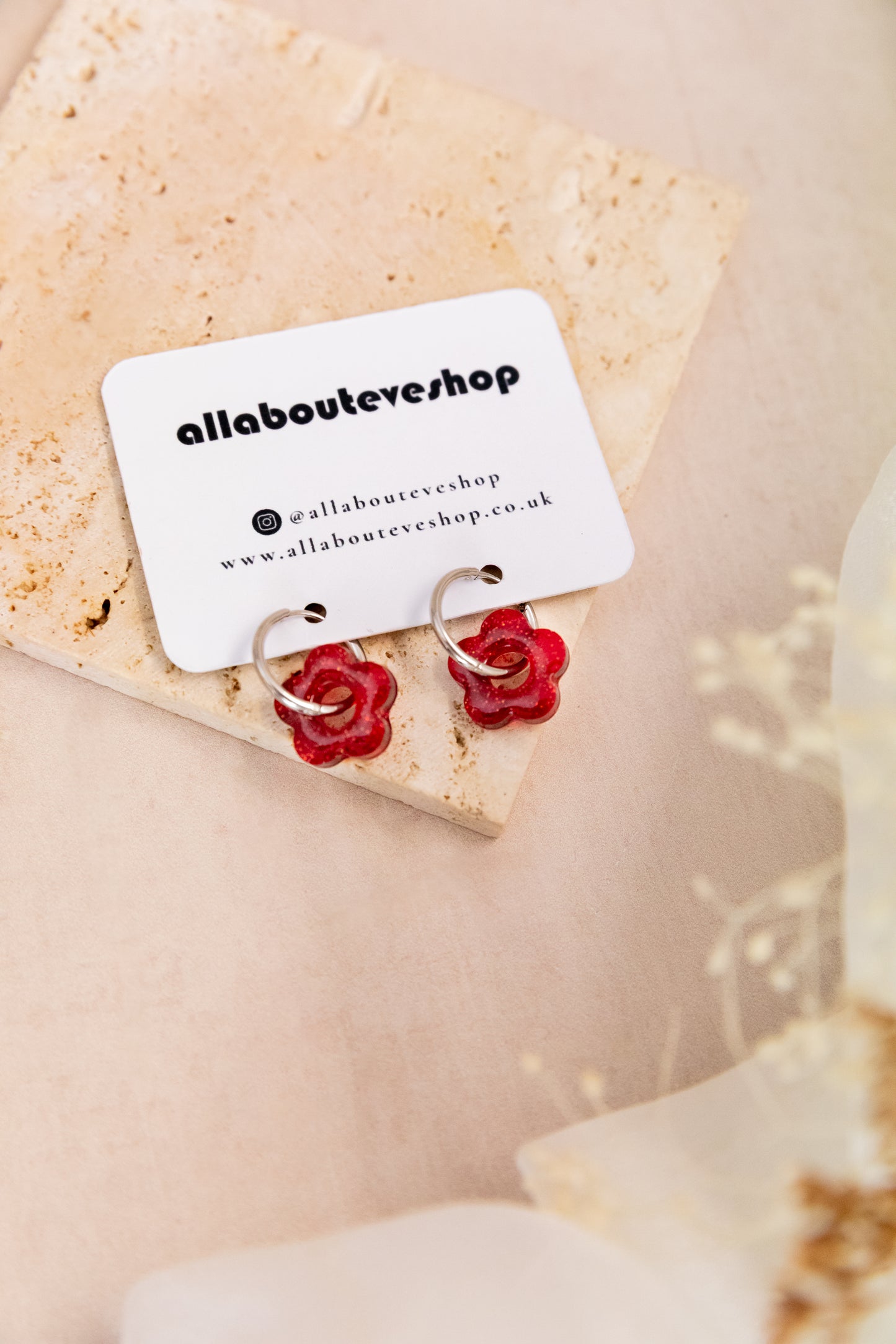Red rose-shaped earrings on a branded card with a beige background