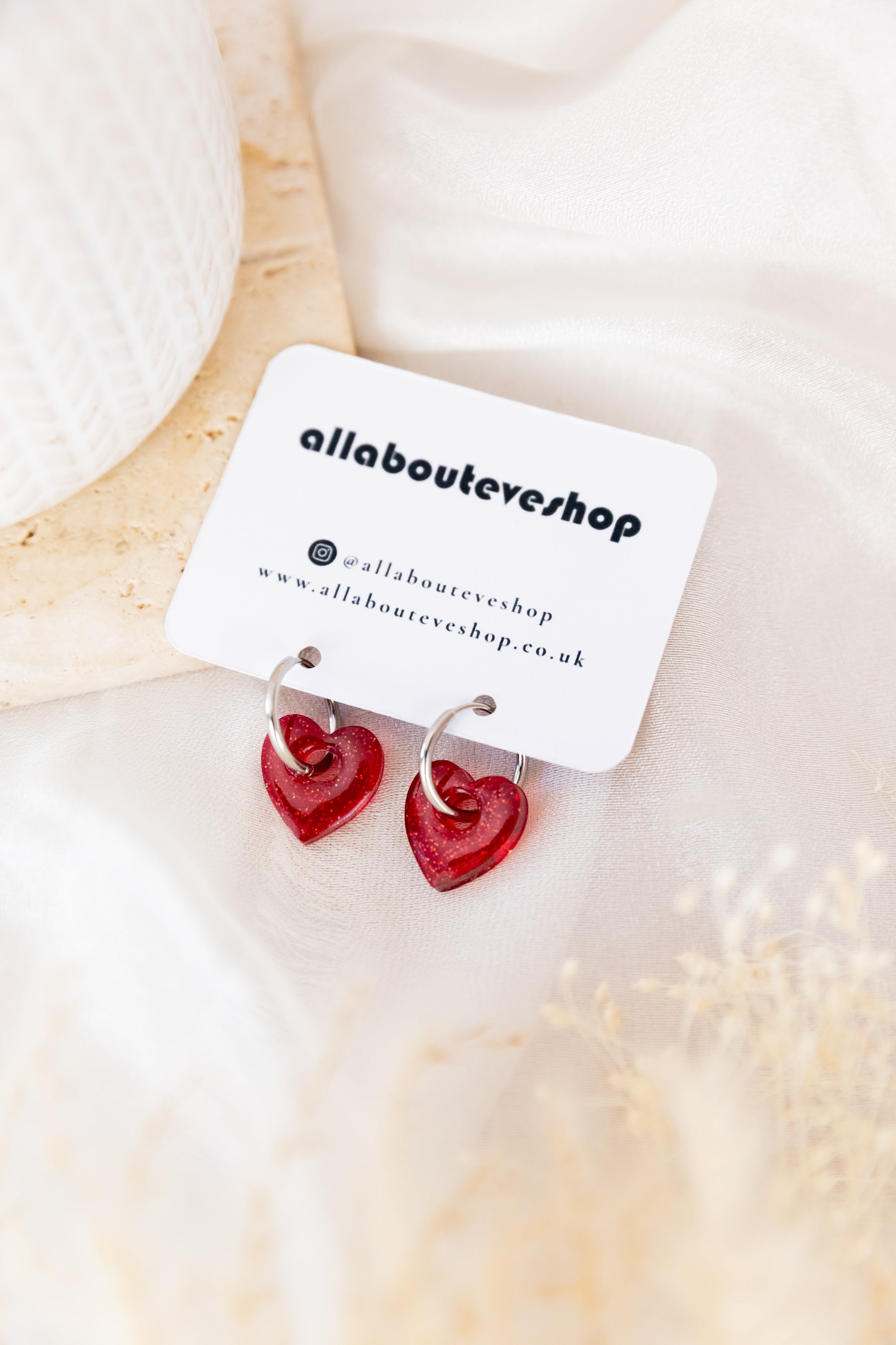 Red heart-shaped earrings on a 'allabouteve' branded card against a soft beige background.