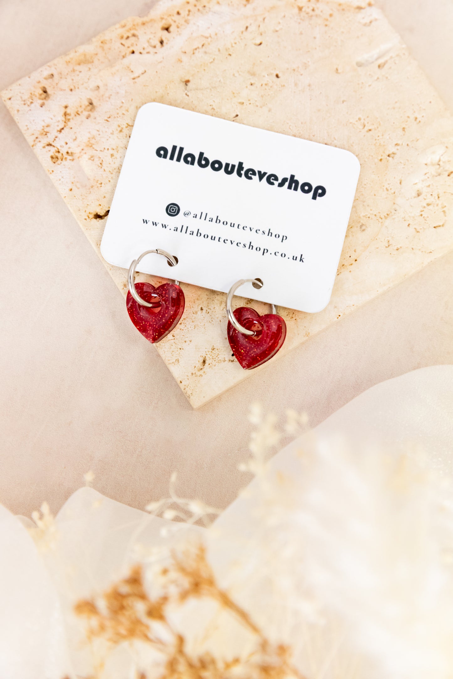Heart-shaped earrings on a card with 'allabouteveeshop' branding on a beige background.