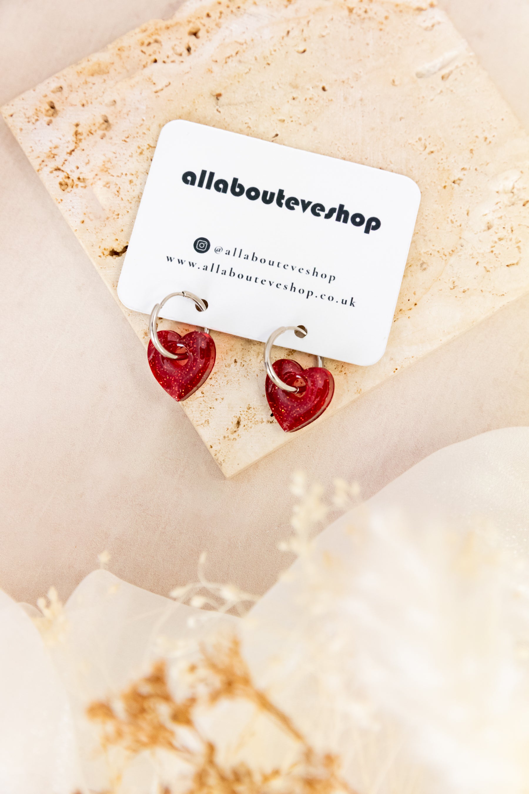 Heart-shaped earrings on a card with 'allabouteveeshop' branding on a beige background.