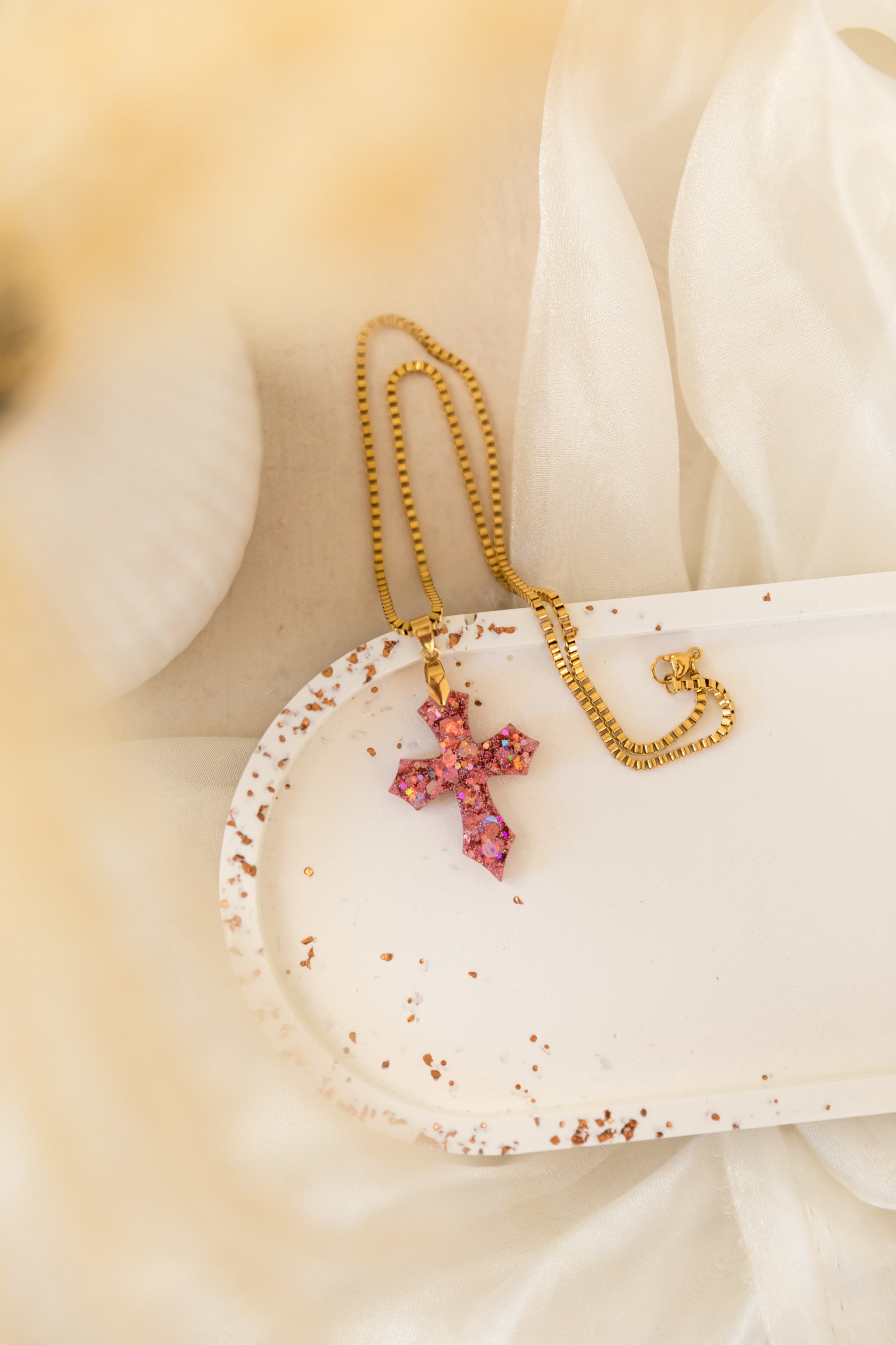 Necklace with a pink cross pendant on a white shell against a soft beige background